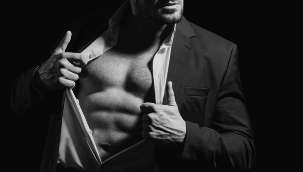 Fashionable young man wearing suit posing over black background. Handsome man posing in white shirt and dark blue suit. Sexy naked torso, six pack abs with open shirt - 写真・画像