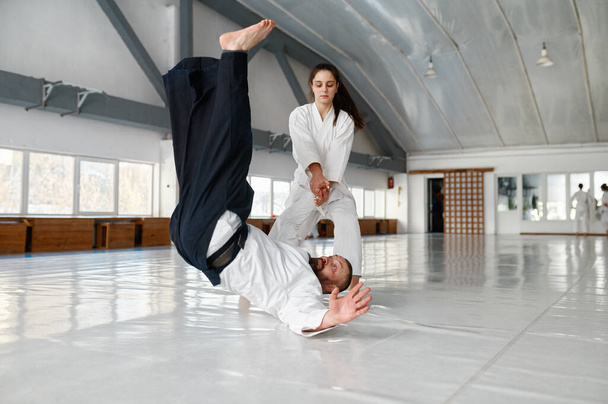 Getalenteerde vrouwelijke student gooien aikido leraar op de vloer tijdens sparring en zelfverdediging training in de sportschool - Foto, afbeelding