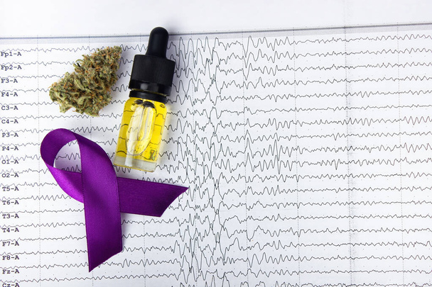 Vor dem Hintergrund der Ergebnisse der Elektroenzephalographie liegen eine Glasflasche mit cbd-Öl neben einer trockenen Knospe medizinischen Marihuanas und einem lila Schleifensymbol. Alternative Behandlungen gegen Epilepsie - Foto, Bild