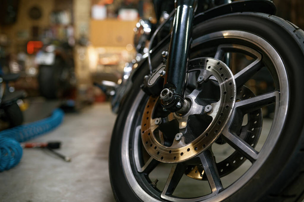 Closeup view on motorcycle front wheel in workshop. Motorbike showroom for sale or repair garage service concept - Foto, afbeelding
