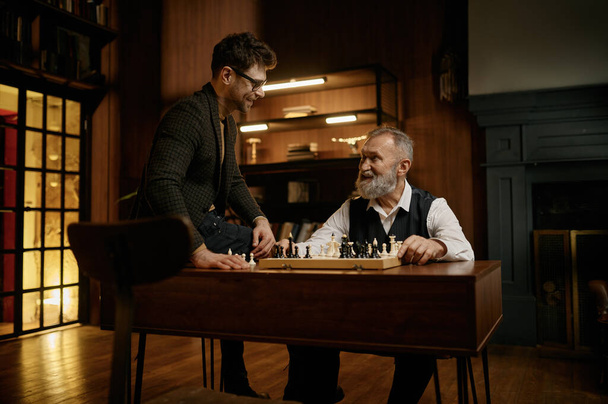 Happy älykäs perhe pelaa shakkia viettää aikaa yhdessä kotona kirjastossa. Lämmin suhde vanhempi isä ja nuorempi poika - Valokuva, kuva