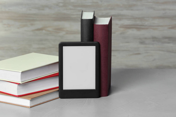 Portable e-book reader and many hardcover books on white textured table, space for text - Foto, imagen