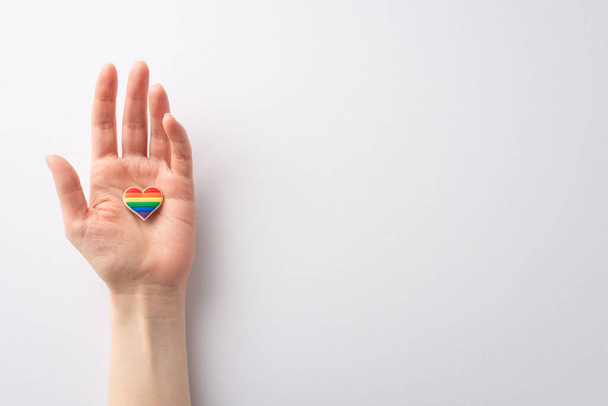 První osoba shora pohled mladá žena ruka drží srdce ve tvaru pin odznak na bílém pozadí s prázdným prostorem pro text nebo inzerát, připomínající LGBTQ Historie měsíc - Fotografie, Obrázek