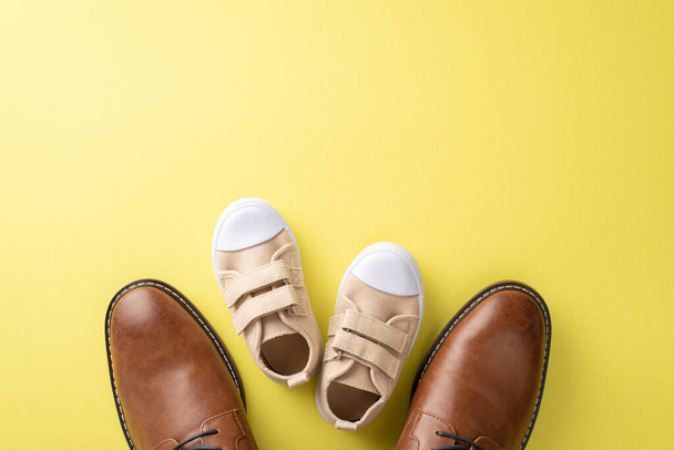 Vaderdag vieren met vader en zoon. Bovenaanzicht van lederen schoenen, en baby sneakers op gele achtergrond met lege ruimte voor reclame of boodschap - Foto, afbeelding