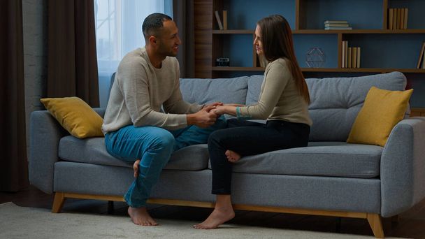 Multiracial pari rakastunut perhe mies aviomies puhua naisen kanssa vaimo pitää kädestä tukeva suhde hoito romanttinen läheisyys päivämäärä istua sohvalla olohuoneessa tyttö kaveri puhuu tarjouksen suhteita - Valokuva, kuva