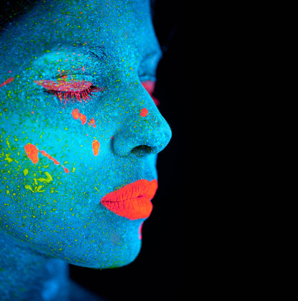 Neon paint, makeup and woman face with beauty closeup in dark background and creative cosmetics. Glow, fantasy and psychedelic cosmetic of female model with unique and creativity with art in studio. - Foto, Imagem