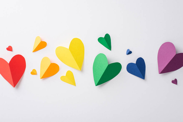 Overhead shot of LGBT support accessories, such as paper hearts in rainbow colors, arranged on a white surface - Фото, изображение