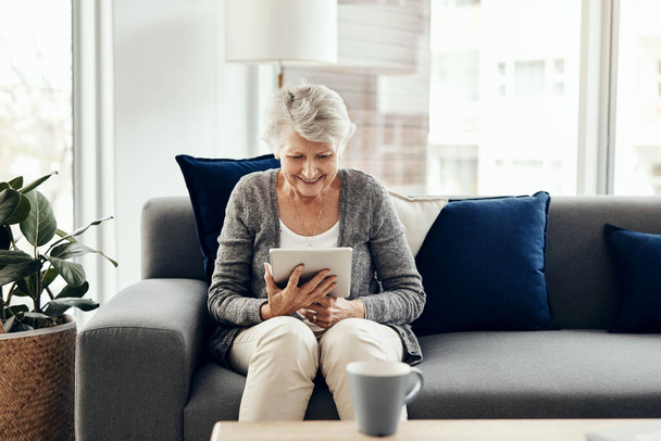 Технически подкованная бабушка гораздо более вовлечена в это. пожилая женщина с помощью цифрового планшета во время отдыха дома - Фото, изображение