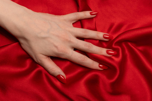 Женская рука с красными ногтями пытается сорвать красную шелковую ткань.  - Фото, изображение