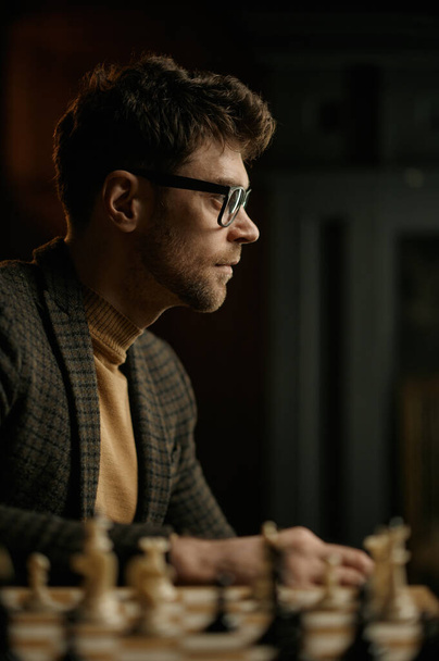 Πορτρέτο του νεαρού παίκτη σκάκι κάθεται στο τραπέζι με σκακιέρα - Φωτογραφία, εικόνα