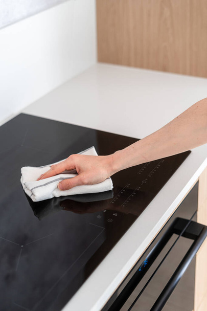 bijgesneden schot van vrouwelijke handdoek en schoonmaken inductie glas keramische kookplaat in de keuken, huishoudelijke klusjes concept - Foto, afbeelding