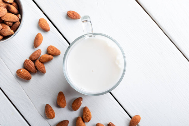 Glass of almond milk and nuts on white background, top view. Almond milk in glass and almond nuts on a wooden background. - Fotó, kép