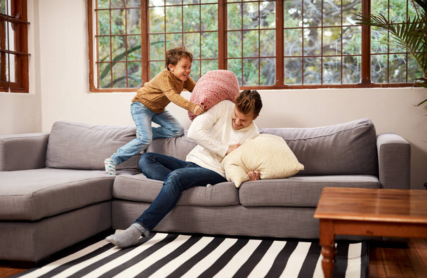 Это мелочи, которые делают их детство забавным. мужчина и его маленький сын дерутся подушками на диване дома - Фото, изображение