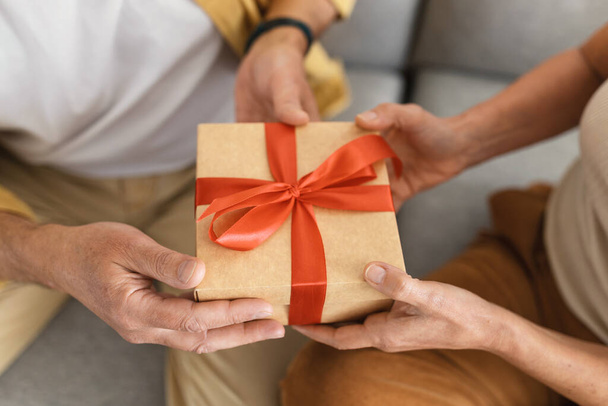 Unrecognizable senior male and female hands holding wrapped paper gift box with red bow, aged spouses celebrating valentine day or anniversary, cropped shot, closeup - Fotoğraf, Görsel