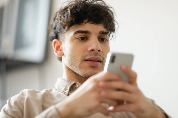 Mobile Offer. Portrait Of Arabic Guy Surfing Internet On Smartphone Communicating And Having Fun Online Indoors. Gadget Leisure And Social Media Apps Advertisement Concept. Selective Focus - 写真・画像