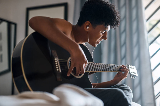 How it sounds is how you feel. a young man using earbuds while playing the guitar at home - Photo, Image