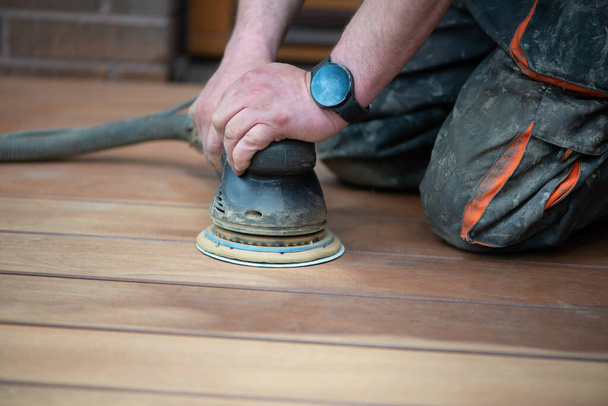 Schuurproces van houten terrasvloeren. Schuurmachine verwijdert onvolkomenheden. Verjonging en onderhoud van houten buitenvloeren, restauratie van hout. - Foto, afbeelding
