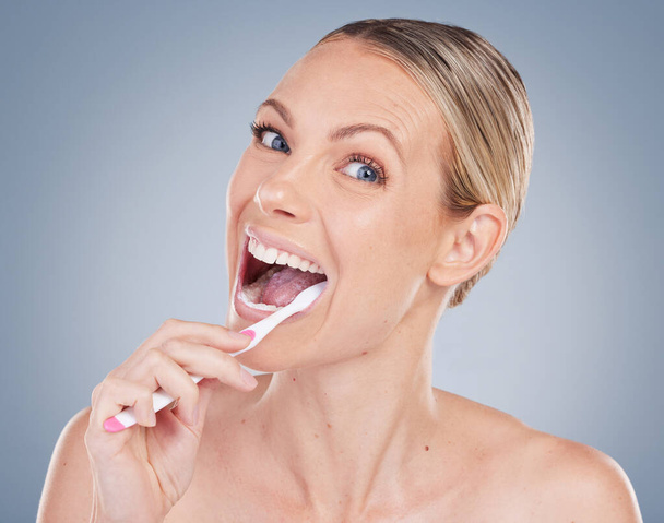 Борьба с кариесом. Студийный портрет привлекательной молодой женщины, чистящей зубы на сером фоне - Фото, изображение