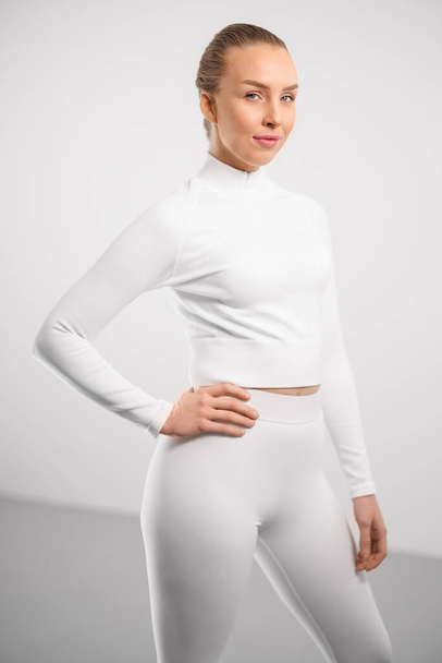 Portrait of smiling young woman in athleisure standing with hand on hip against white background - Fotografie, Obrázek