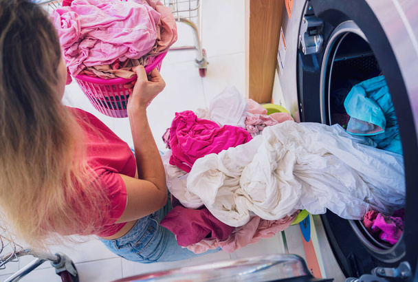 Young beautiful woman washes and dries clothes in the laundry. - Фото, изображение