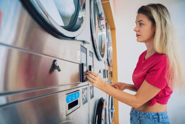 Young beautiful woman washes and dries clothes in the laundry. - Photo, image