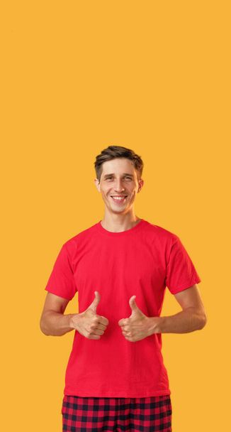 Approval gesture. Nice job. Great achievements. Attractive happy satisfied man in red showing like sign smiling isolated on yellow empty space background. - 写真・画像