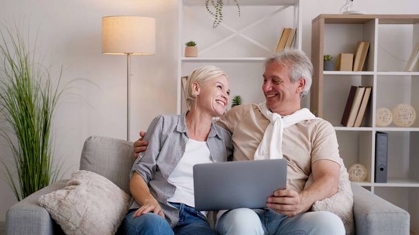 Family leisure. Happy couple. Online movie. Excited middle-aged man and woman sitting sofa with laptop in light home interior. - Valokuva, kuva