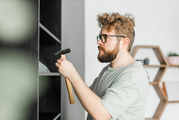 Junger attraktiver Mann montiert Möbel - Handarbeit und Einrichtungsgegenstände - Foto, Bild