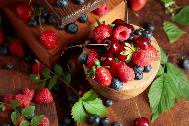 Verschiedene frische Beeren mit Blättern. Erdbeeren, Himbeeren, Blaubeeren und Süßkirschen auf einem alten Jahrgangstisch.  - Foto, Bild