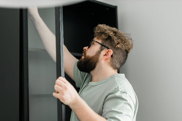 Bearded millennial man assemble his bookcase. He uses tools for furniture. Furniture for the interior room apartments - Φωτογραφία, εικόνα