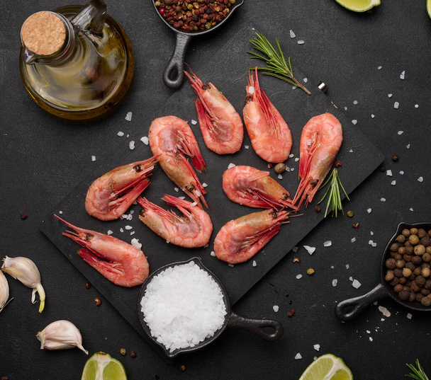 Boiled shrimp on a board, lemon slices, spices on a black background, top view - Photo, Image