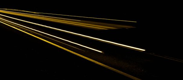 Goldene Linien von Autoscheinwerfern auf schwarzem Hintergrund - Foto, Bild