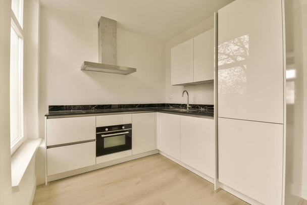 une cuisine avec armoires blanches et comptoirs noirs sur les comptoirs en face du four, qui est monté dans le mur - Photo, image