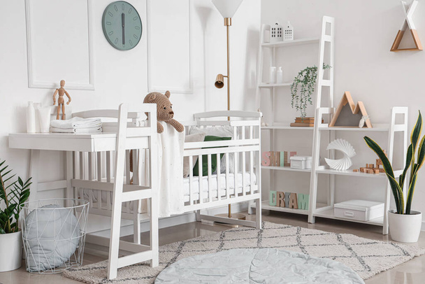 Interior of light bedroom with baby crib, changing table and shelving unit - 写真・画像