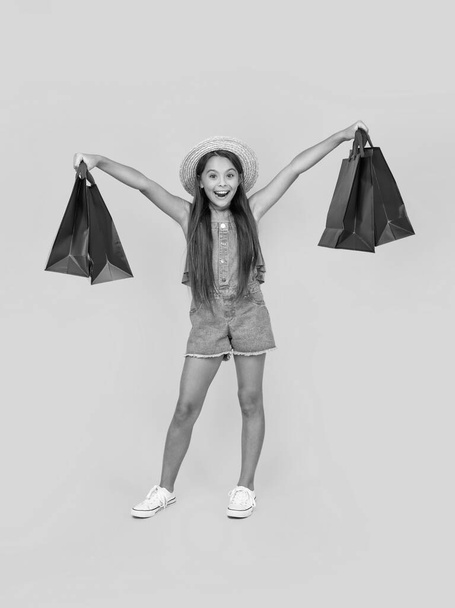 amazed teen child with shopping bags on yellow background. full length. - Zdjęcie, obraz