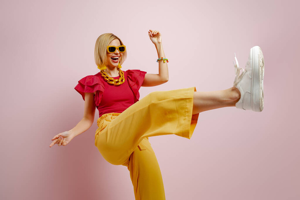 Full length of excited young woman in vibrant clothes dancing against colored background - Фото, зображення