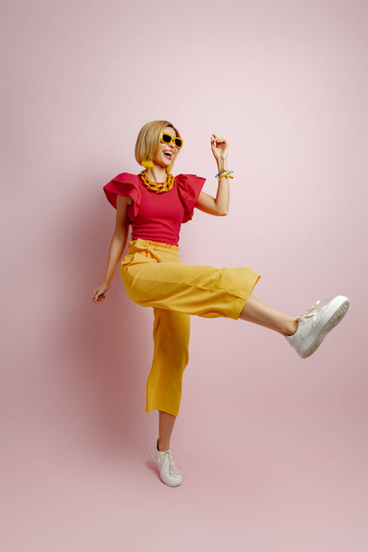Full length of excited young woman in vibrant clothes dancing against colored background - Photo, Image