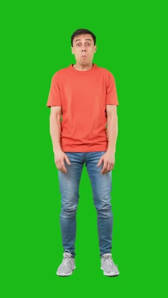 Pełne ciało zdumiony model męski w ubraniu casual patrząc na aparat z zdezorientowanej twarzy, odizolowany na zielonym tle w studio - Materiał filmowy, wideo