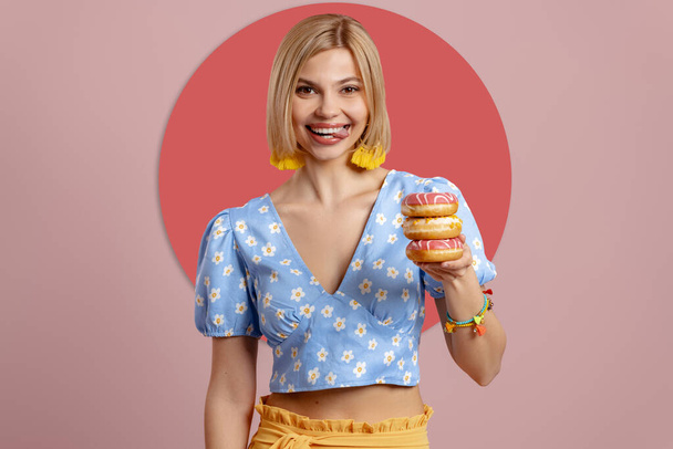 Playful young woman holding doughnuts and sticking out tongue against pink background - Photo, Image