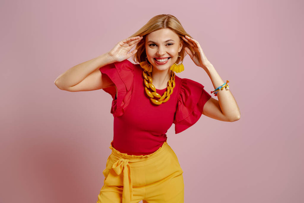 Fashionable young woman pointing camera and smiling against pink background - Photo, Image