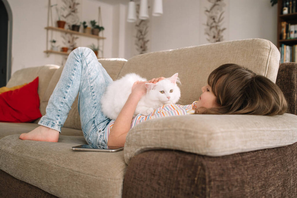 Egy tinédzser lány játszik a szeretett fehér, bolyhos cicájával. Háziállatok iránti szeretet és gondoskodás. Háziállatok élete a lakásban. - Fotó, kép