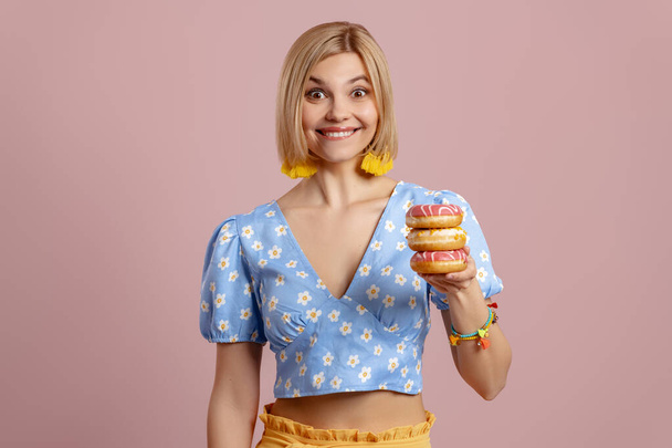 Excited young woman holding doughnuts and smiling against pink background - Photo, Image