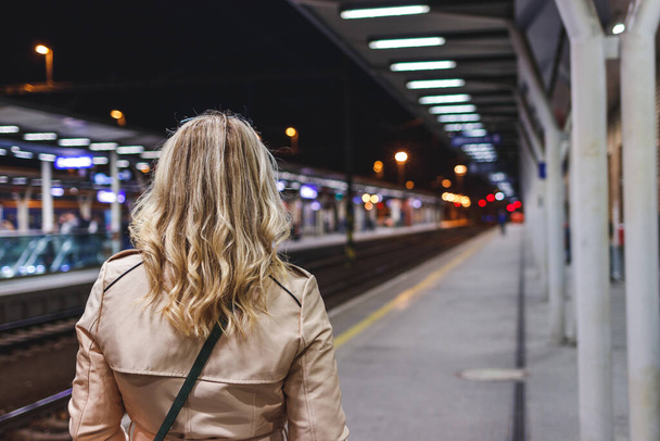 Γυναίκα περιμένει το τρένο στο σιδηροδρομικό σταθμό. Μέσα μαζικής μεταφοράς. Ο μεταφορέας ταξιδεύει με τρένο. Ζωή στην πόλη τη νύχτα - Φωτογραφία, εικόνα