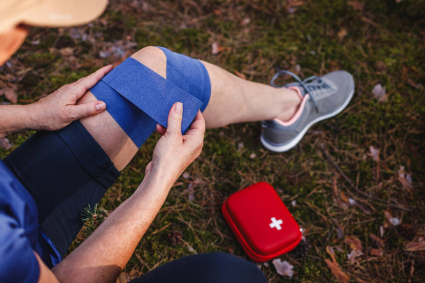 Fissazione della distorsione del ginocchio durante le escursioni. Donna ferita con benda elastica dal kit di pronto soccorso - Foto, immagini