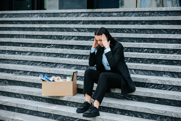 A woman sits on the stairs with a pensive expression, contemplating the impact of her work loss on her career and future prospects. Depressed Brunette Sitting Outdoors After Job Loss - Foto, Imagen
