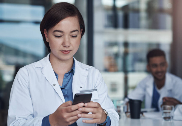Felhívhatlak valamikor? egy fiatal női orvos, aki az okostelefonját használja SMS küldésére - Fotó, kép