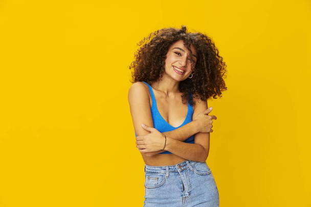 Femme avec des cheveux afro frisés dans un t-shirt bleu. signes de fond jaune avec ses mains, regarder dans l'appareil photo, sourire avec les dents et le bonheur, copier l'espace. Photo de haute qualité - Photo, image