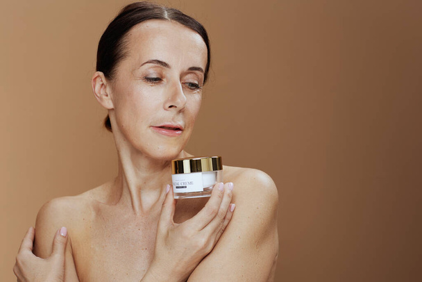 modern middle aged woman with facial cream jar on beige background. - Zdjęcie, obraz