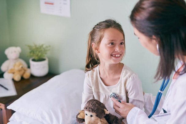 Medical, children and a girl at the pediatrician for an appointment or checkup in the hospital. Healthcare, stethoscope and cardiology with an adorable female child sitting on a bed in the clinic. - Photo, Image