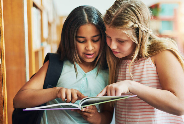 Ez az a kérdés, amiről beszéltél. két fiatal iskolás lány együtt olvas egy könyvet, miközben napközben egy osztályteremben állnak. - Fotó, kép